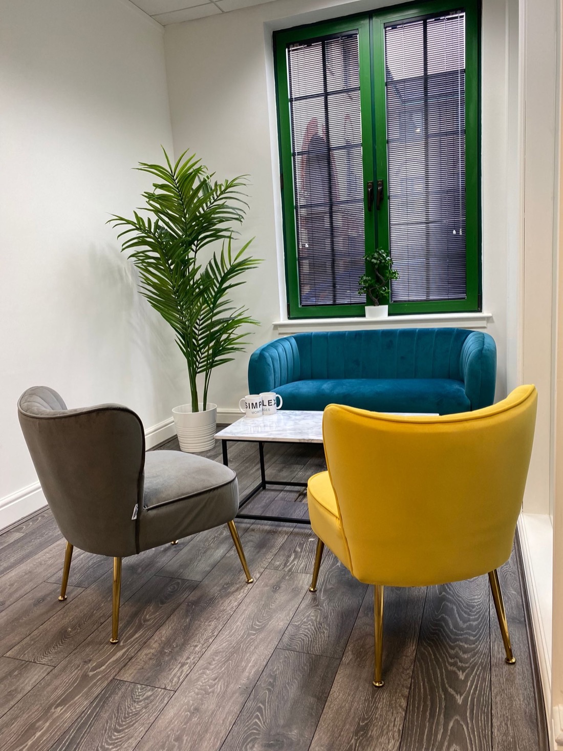 The Simplex Mortgages meeting room in Woodford Green, teal velvet sofa, mustard armchair and a branded Simplex mug on a marble table
